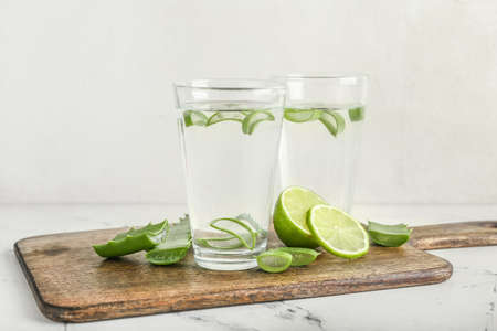 Board with glasses of aloe juice and leaves on white background