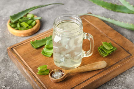 Board with glass of aloe juice, spoon and leaves on grunge backgroundの写真素材
