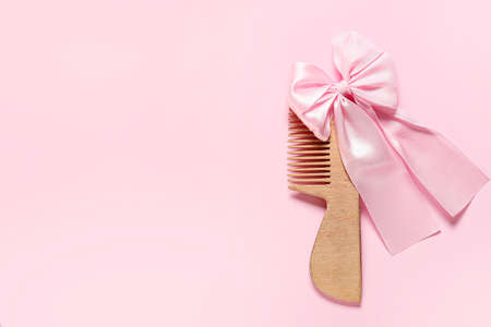 Wooden comb for baby and hair bow on pink background