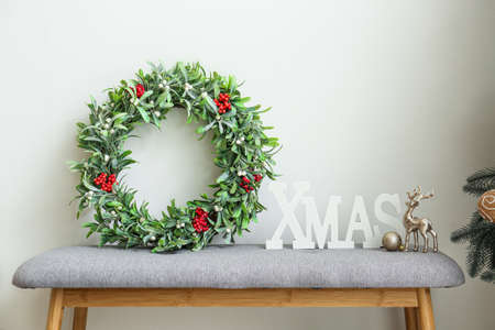 Beautiful mistletoe wreath with Christmas decor on bench in roomの写真素材