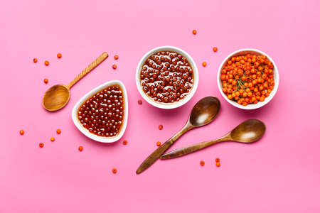 Composition with tasty rowan jam, berries and spoons on color backgroundの写真素材