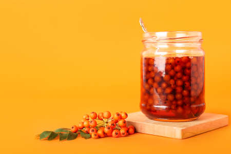 Glass jar with tasty rowan jam on color backgroundの写真素材
