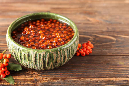 Bowl of tasty rowan jam on wooden background