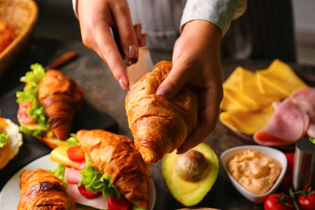 Woman preparing tasty croissant sandwich at kitchen tableの写真素材