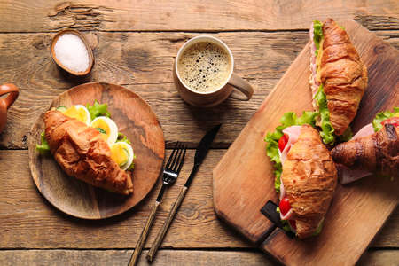 Board and plate with delicious croissant sandwiches and cup of coffee on wooden backgroundの写真素材
