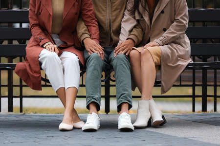 Man and two beautiful women sitting on bench in park. Polyamory conceptの写真素材