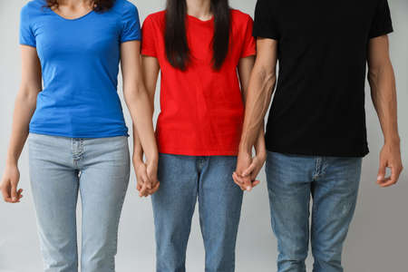 Man and two beautiful women on gray background. Polyamory concept