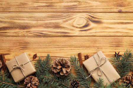 Fir tree branches, gift boxes, pine cones, cinnamon and anise on wooden background
