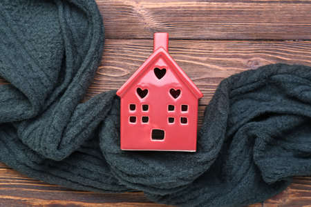 House figure with warm scarf on dark wooden background. winter conceptの写真素材