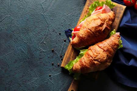 Wooden board with delicious croissant sandwiches on black backgroundの写真素材