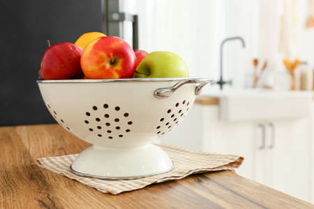 Colander with fruits on wooden table top in kitchenの写真素材