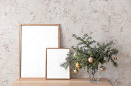 Vase with Christmas tree branches and blank photo frames on table near light wallの写真素材