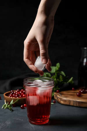 Woman putting ice cube into glass with healthy cranberry juice on dark backgroundの写真素材