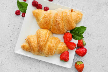 Plate of delicious croissants with berries on light backgroundの写真素材