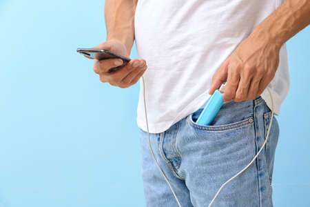 Young man with phone and power bank on color backgroundの写真素材