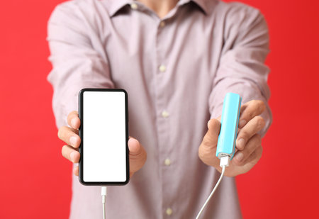 Young man with phone and power bank on color background, closeupの写真素材