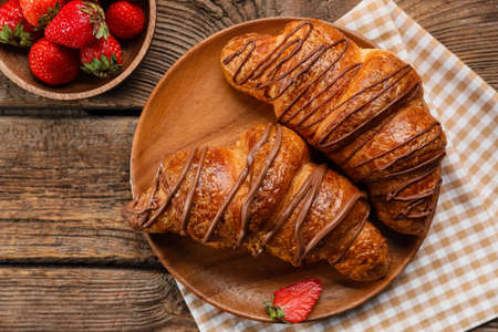 Plate of delicious croissants with chocolate and strawberry on wooden backgroundの写真素材