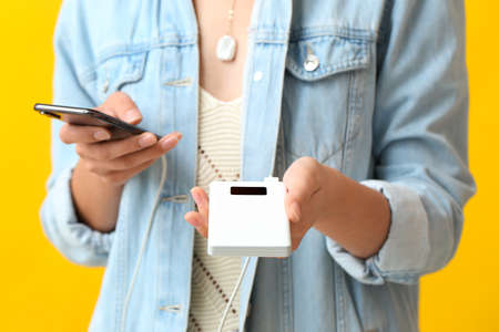 Young woman with phone and power bank on color backgroundの写真素材