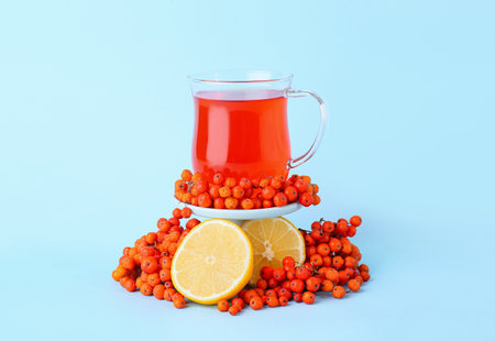 Composition with cup of tasty rowan tea, lemon and berries on blue backgroundの写真素材
