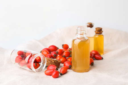 Bottles of essential oil and rose hip berries on light backgroundの写真素材