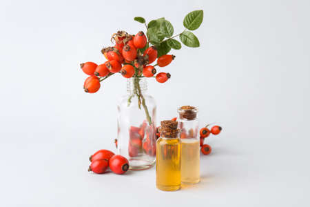 Bottles of essential oil and rose hip berries isolated on white backgroundの写真素材