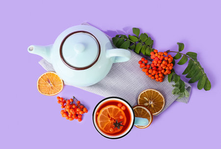 Composition with cup and teapot with hot rowan tea on lilac backgroundの写真素材