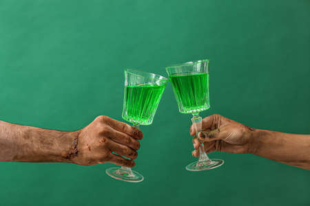 Hands of zombies with glasses of cocktail on color backgroundの写真素材