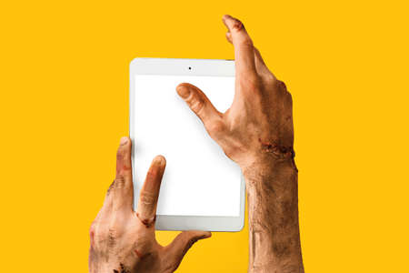 Hands of zombie with tablet computer on color background