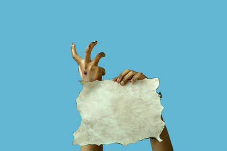 Hands of zombie with empty paper sheet on color backgroundの写真素材
