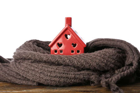 Toy house with warm scarf on table against white background. winter conceptの写真素材