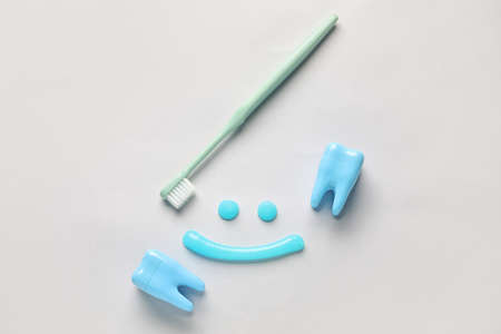 Smile made of toothpaste, brush and plastic teeth on light background