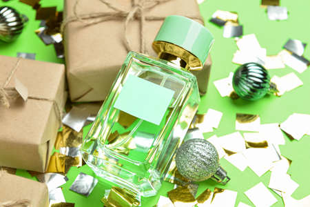 Perfume bottle, gift boxes, Christmas balls and confetti on color background, closeup