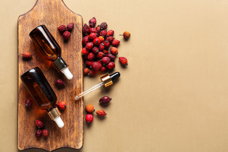 Wooden board with bottles of essential oil and dried rose hip berries on color backgroundの写真素材