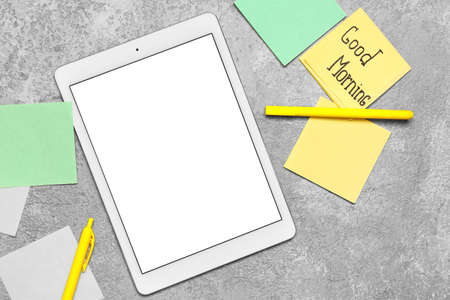 Composition with tablet computer and sticky notes with text GOOD MORNING on gray background