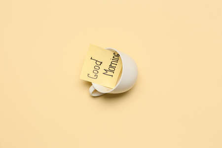 Sticky note with text GOOD MORNING in cup on color backgroundの写真素材