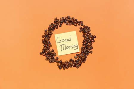 Frame made of coffee beans and sticky note with text GOOD MORNING on color background