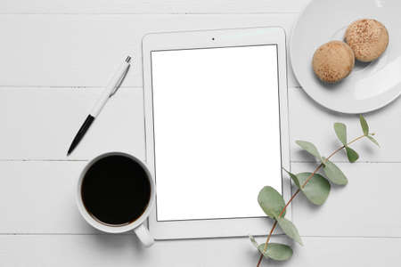 Composition with tablet computer, cup of coffee, macaroon, pen and eucalyptus branch on white wooden backgroundの写真素材