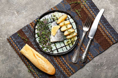 Plate of tasty sea bass fish with vegetables and bread on grunge backgroundの写真素材