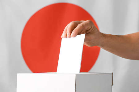 Voting man near ballot box against flag of Japanの写真素材