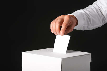 Voting man near ballot box on dark background