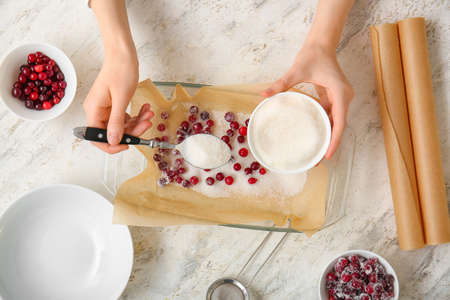 Woman sprinkling sugar onto cranberry on light backgroundの写真素材