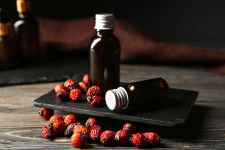Composition with bottles of essential oil and rose hip berries on wooden tableの写真素材