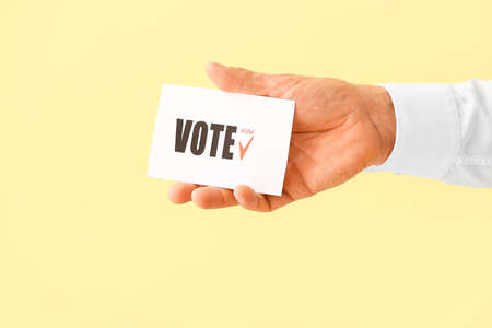 Hand holding paper with text VOTE on color backgroundの写真素材