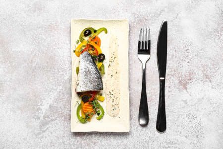 Plate of delicious sea bass fish with vegetables on light background