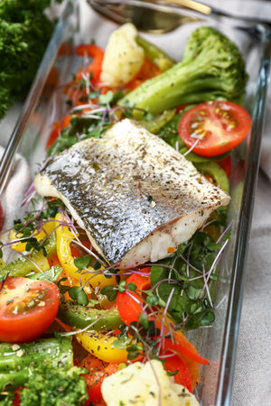 Baking dish of delicious sea bass fish with vegetables on table, closeup