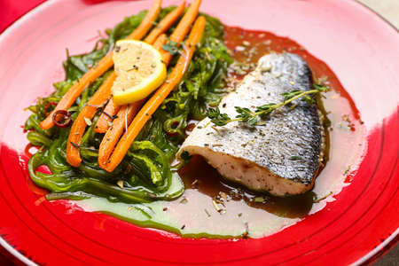 Plate of delicious sea bass fish with vegetables on table, closeup
