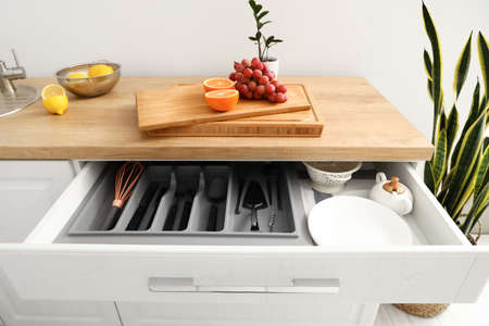 Opened drawer with set of cutlery and fruits on counter in kitchen