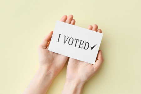 Hands holding paper with text I VOTED on color backgroundの写真素材