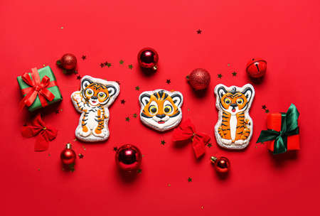 Tasty cookies in shape of tigers and Christmas decorations on red background