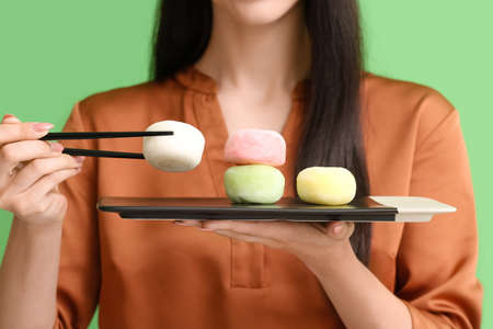 Beautiful young woman with tasty Japanese mochi on color background, closeup